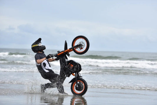 Riding Times GT54 eBike performing a wheelie on the beach with water splashing around