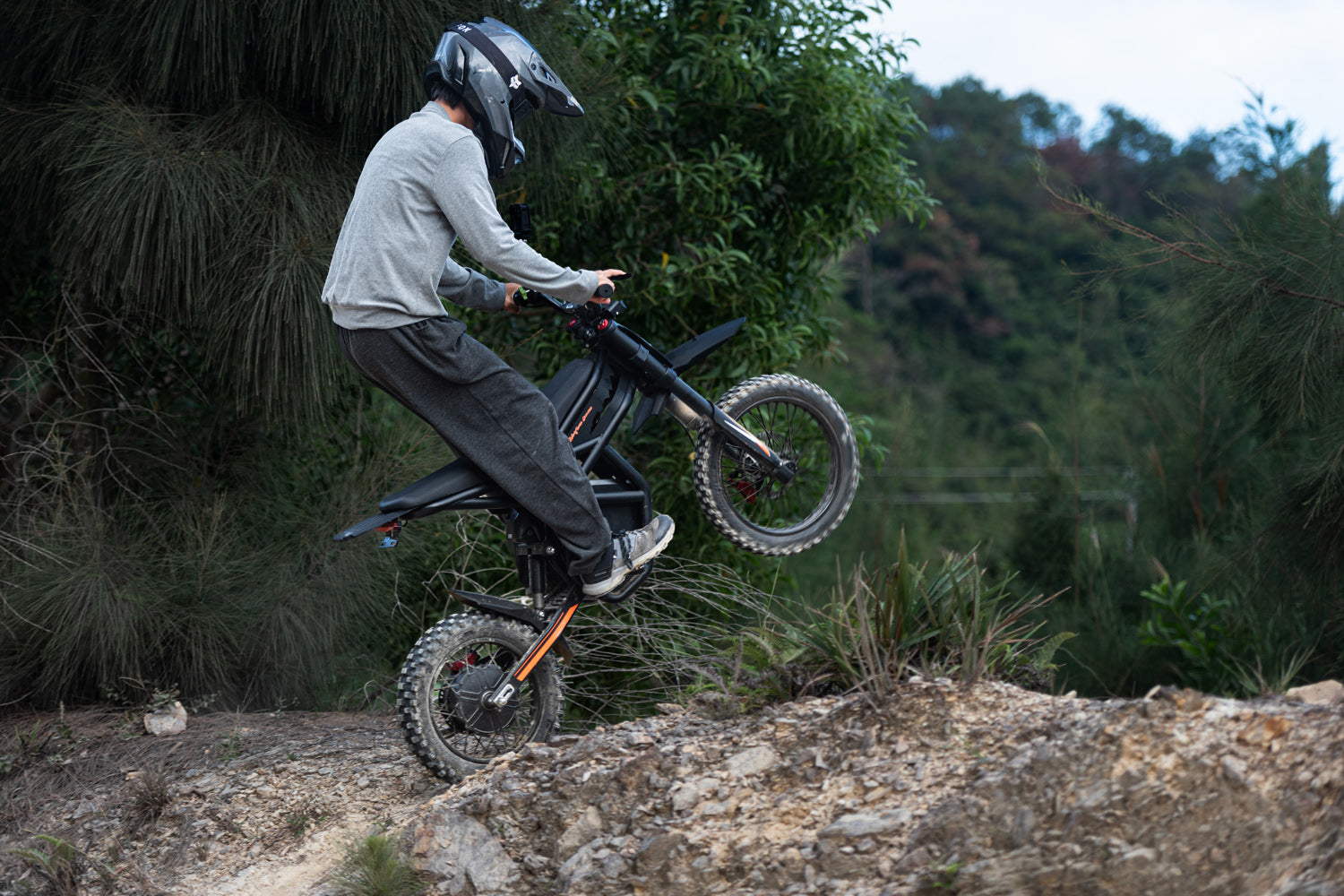 Person riding a GT54 dirt bike on a rocky terrain with trees in the background