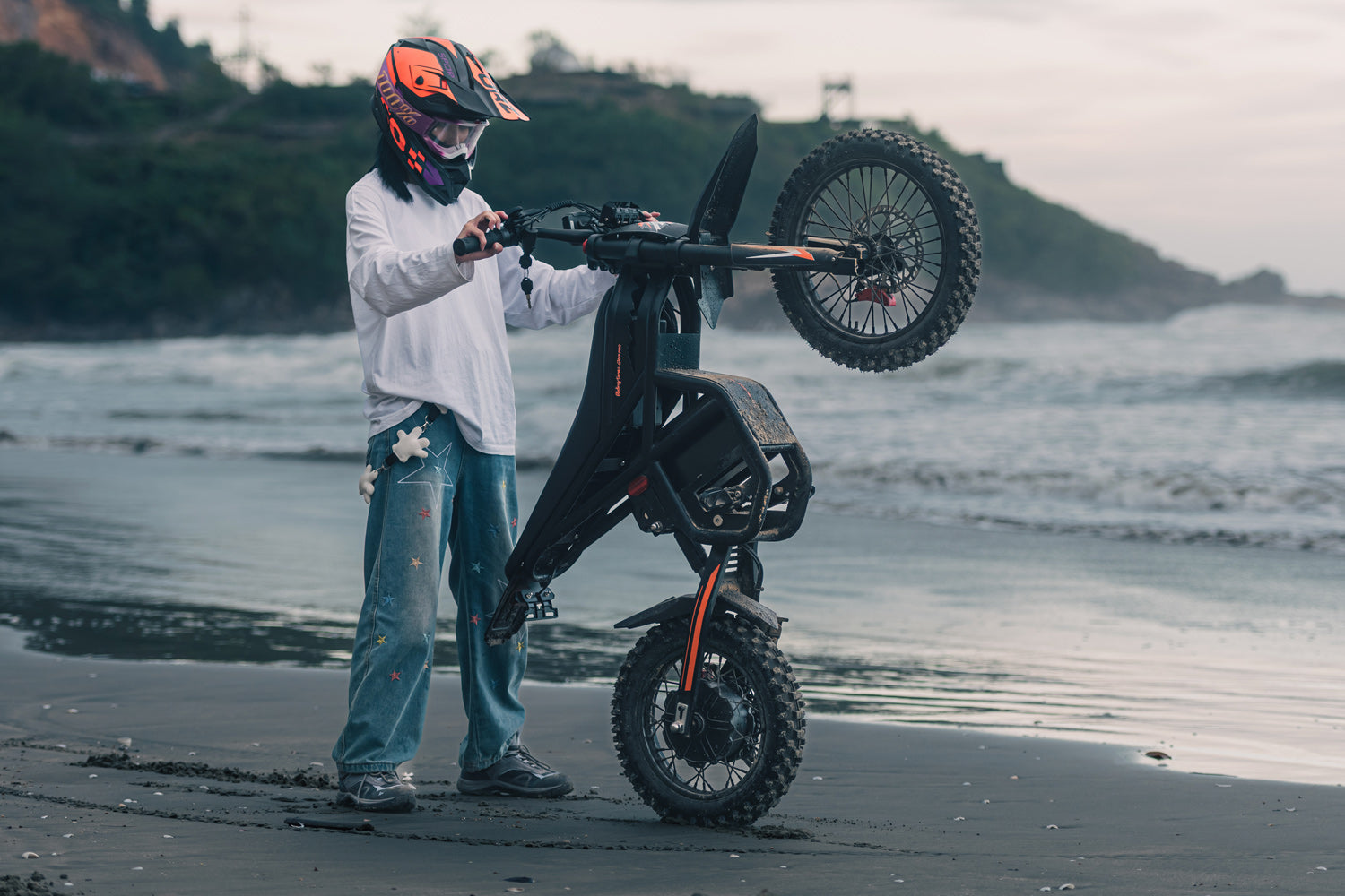 Person with a helmet holding a black GT54Pro off-road vehicle on a beach.