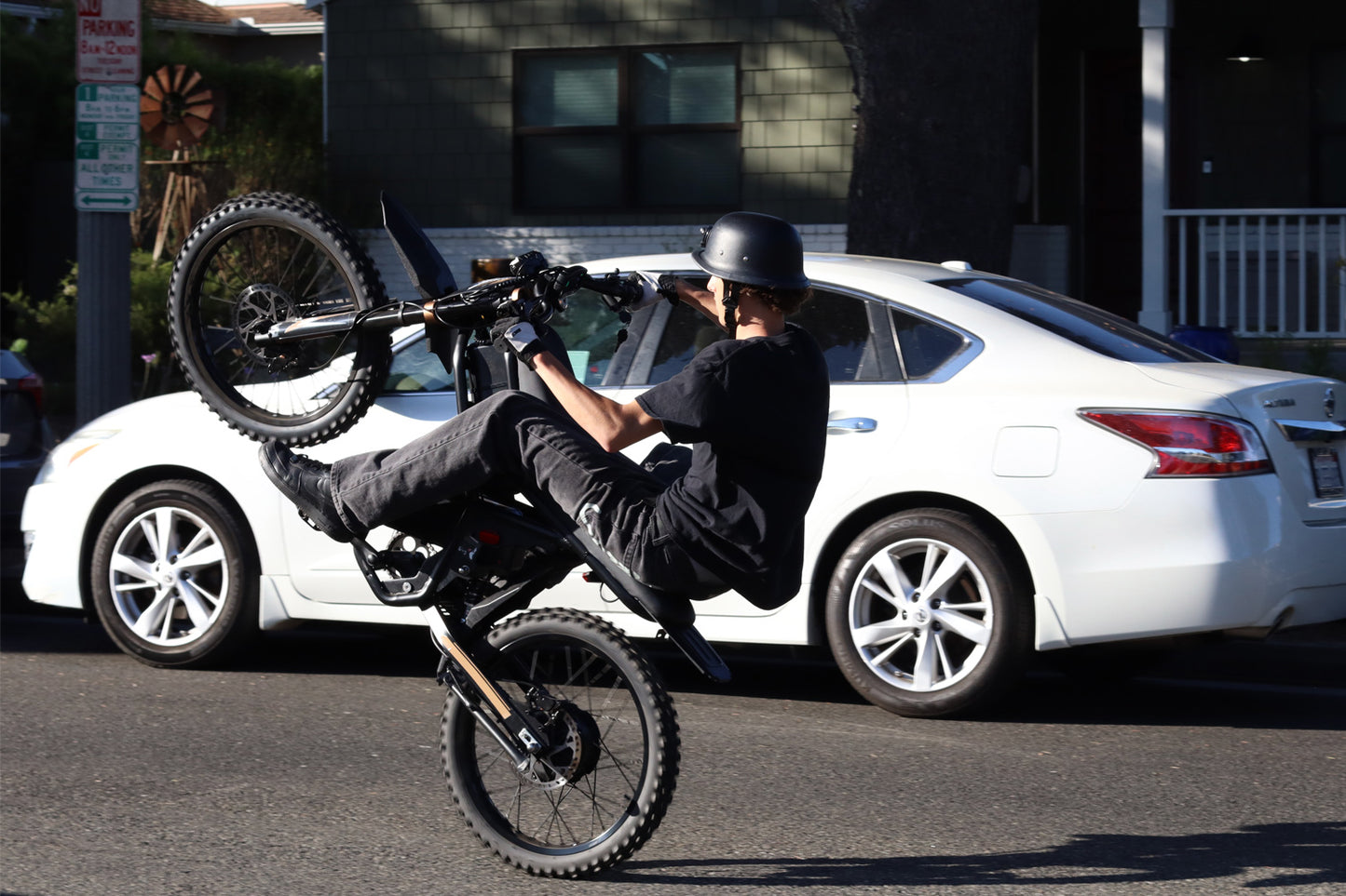 Person performing a wheelie on a GT73Pro Ebike in front of a white car