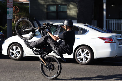 Person performing a wheelie on a GT73Pro Ebike in front of a white car