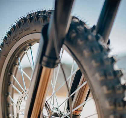 Front Wheel of a dirt bike featuring a black knobby tire and silver metal spokes for off-road traction