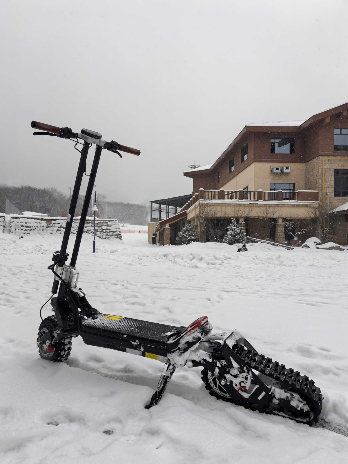 G63 - Convertible Snow Kit with black electric scooter featuring a nylon mesh rubber track and handlebar grips, parked in snow.