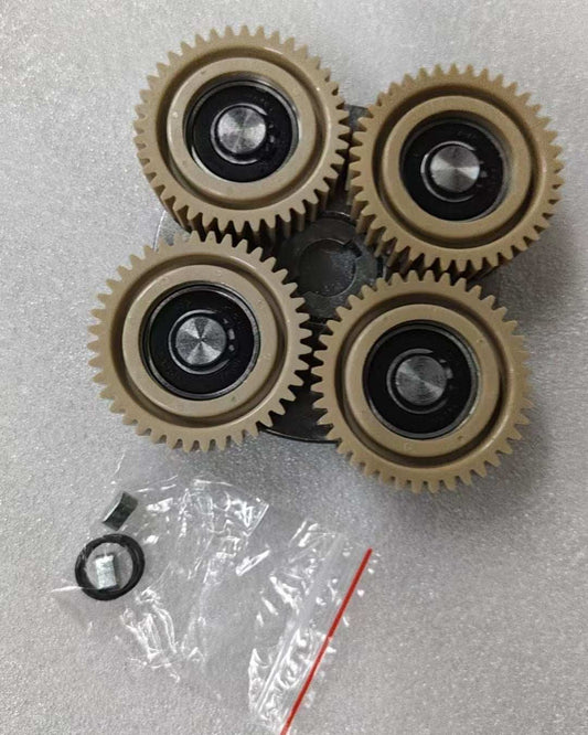 Motor Clutch Assembly featuring four beige plastic gears with black centers arranged on a metal base, including a small plastic bag with extra components