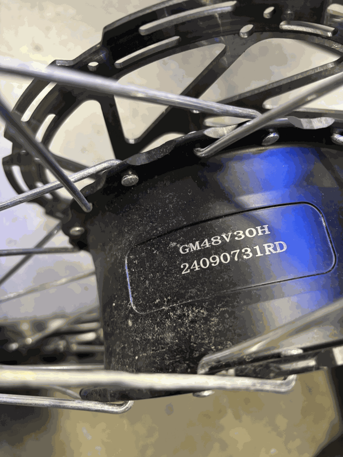 Close-up of a black electric bike motor casing with a serial number GM48V30H 24090731RD visible, surrounded by metal spokes and part of a disc brake rotor